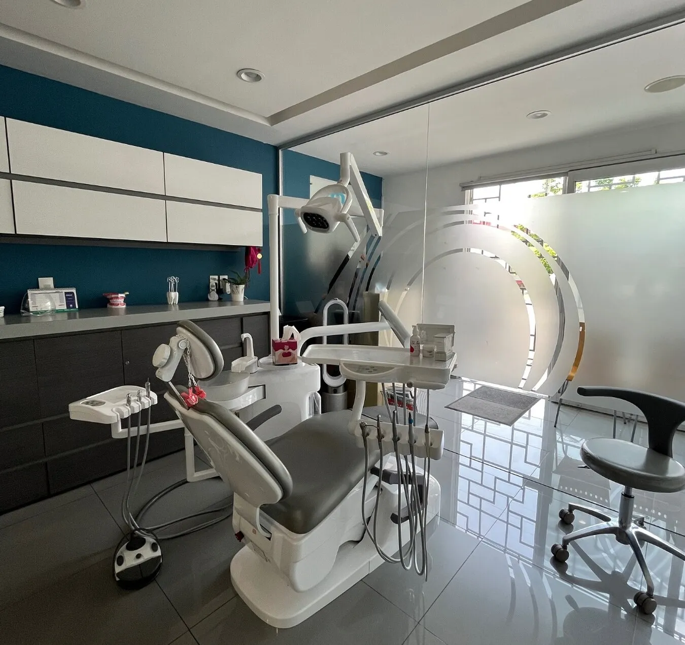 Consultorio con sillón dental, muro azul y paredes de vidrio esmerilado