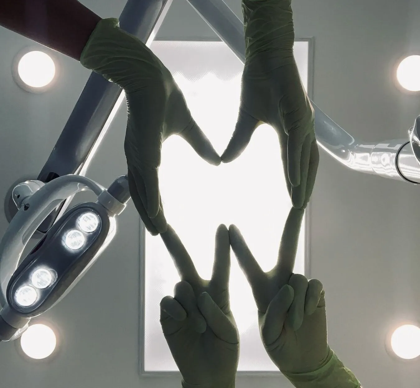 Manos con guantes formando un corazón bajo la lámpara dental